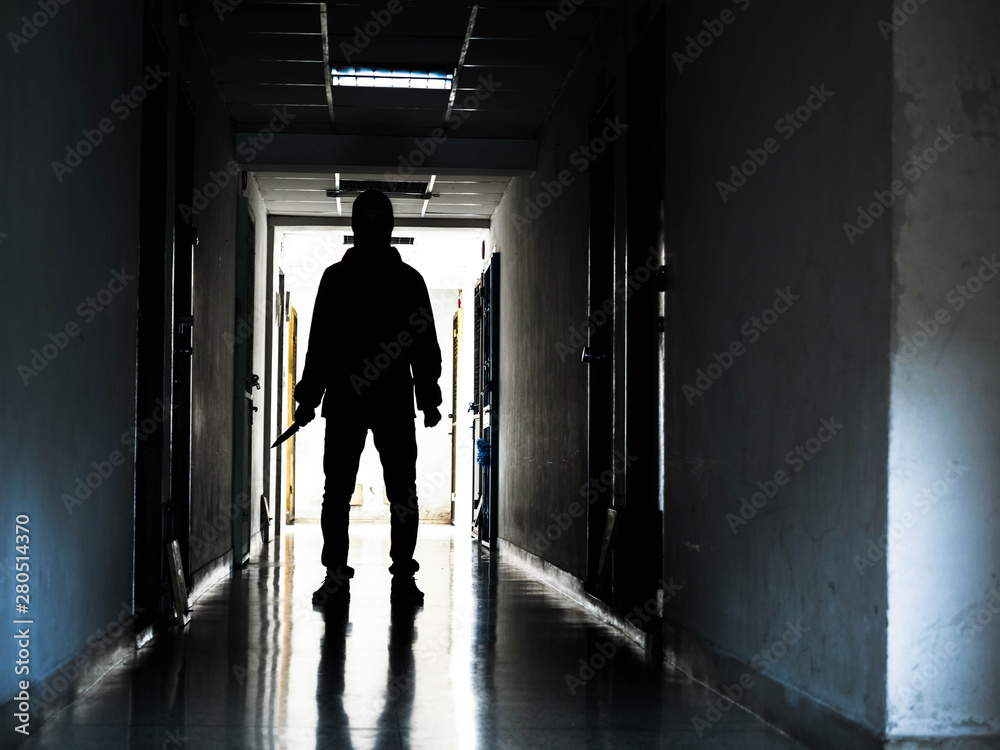 Man silhouette walking away with knife in the light of opening door in dark room, Threat Concept.