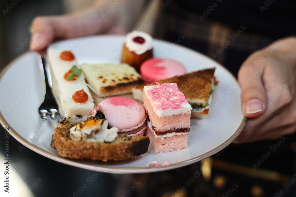 Multiple color sweet desserts cake and macaroon on dish in woman hand Multiple color sweet desserts cake and macaroon on dish in woman hand