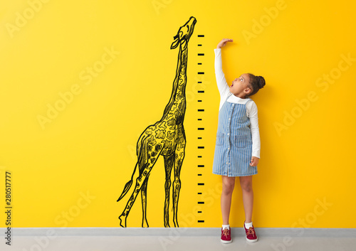 Surprised African-American girl measuring height near color wall with drawn giraffe