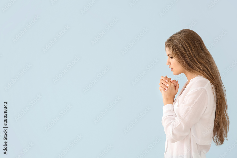 Religious young woman praying to God on light color background Religious young woman praying to God on light color background