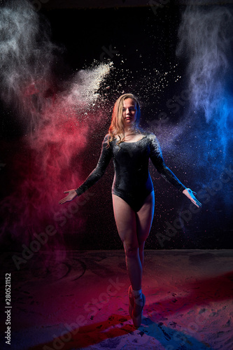 Young teen girl in a dark room during a photoshoot with flour with a colored light and a black background