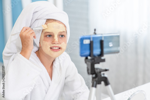 Littlr girl in towel on her head filming the video for her followers about clay facial mask . Kids blogger concept