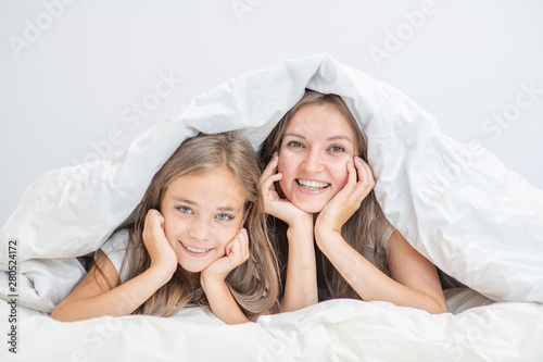 Happy family at home. Smiling mother with daughter lie on the bed under the blanket