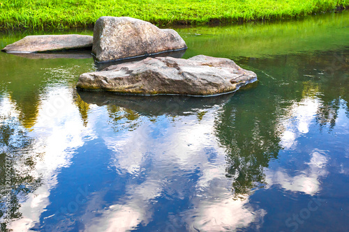 large stones in the river with the reflection of trees