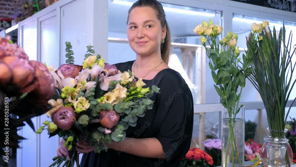 Floral business concept. Florist woman makes big flower bouquet of eucalyptus branches, beige eustoma, brown maroon peony and blue iris and smiles look at camera in flower shop. Floral business concept. Florist woman makes big flower bouquet of eucalyptus branches, beige eustoma, brown maroon peony and blue iris and smiles look at camera in flower shop.