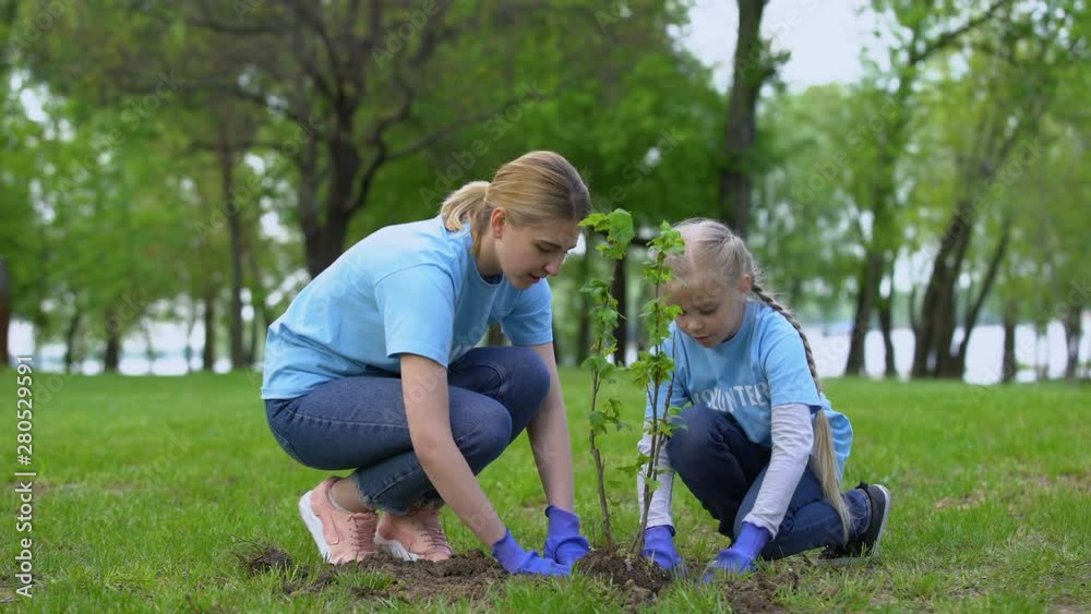 Mother and daughter planting bush in park together, environmental volunteering Mother and daughter planting bush in park together, environmental volunteering