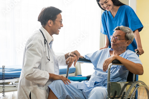 Doctor and physiotherapist talking to elderly patient sitting on wheelchair.