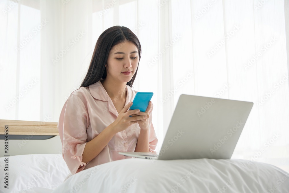 Portrait of smiling beautiful lady wake up viewing mobile phone and working with notebook in morning on the bed with copy space Portrait of smiling beautiful lady wake up viewing mobile phone and working with notebook in morning on the bed with copy space