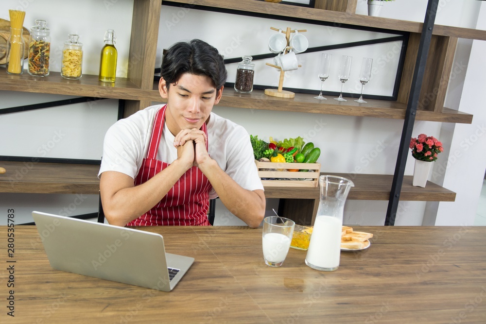 Portrait of healthy adult man in red apron smiling and having breakfast at home kitchen
