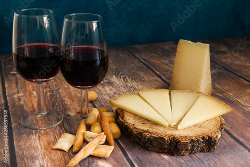 piece and slices of typical Spanish Manchego cheese and two red wine glasses