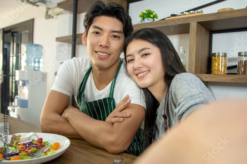 Portrait of cute happy couple in aporn in selfie action posting with mobile phone decorated with salad and orange juice in modern kitchen photo