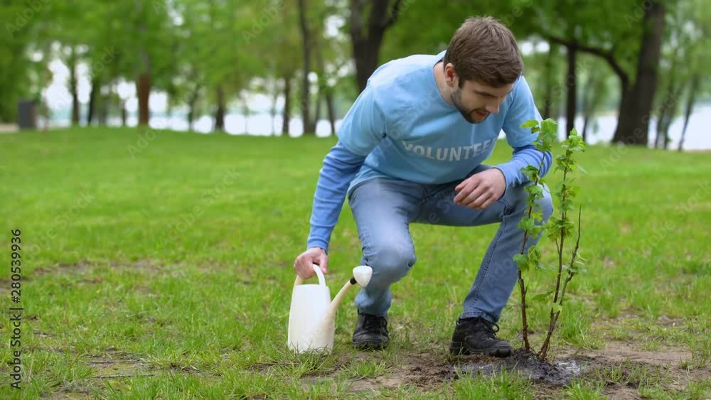 Male eco activist watering tree by can, volunteer taking care natural resources Male eco activist watering tree by can, volunteer taking care natural resources