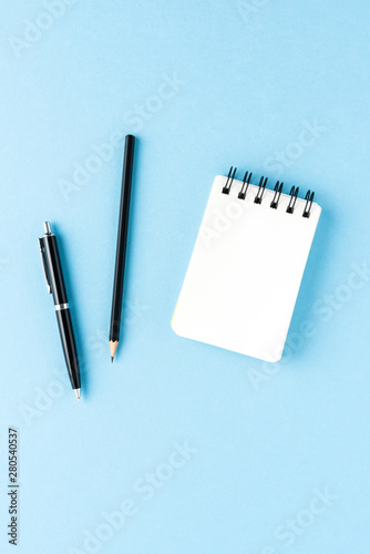 Empty notebook and pens on blue background. Office desktop