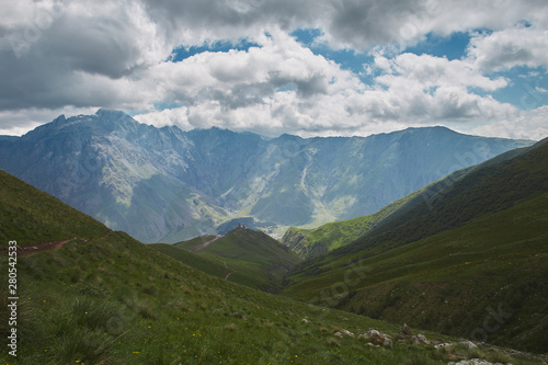 Large scenery of rocky mountains and green hills. Trinity church ahead.Kazbegi Georgia © AlexGo