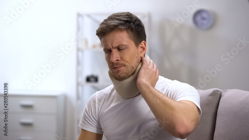 Foto Upset man in foam cervical collar suffering neck pain, rehabilitation center