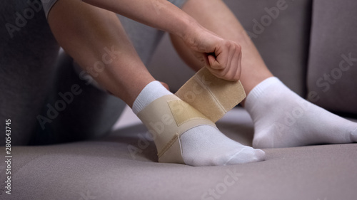 Woman fixing two-strap ankle wrap in proper position, sprained joint, healthcare