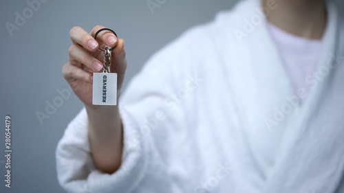 Customer in bathrobe holding keys with Reserved word, booking hotel rooms