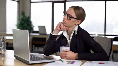 Bored woman having coffee break in office, dissatisfied with work, lack of ideas