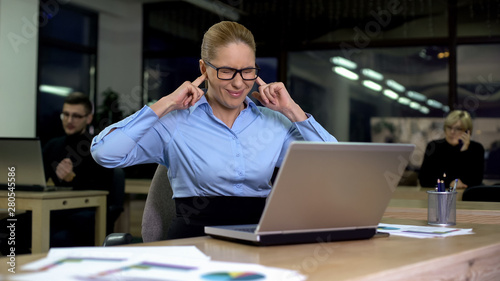 Irritated lady closing ears with fingers, noisy colleagues distracting from work photo