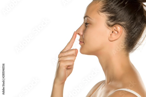 young woman touches her nose with her finger on a white background photo