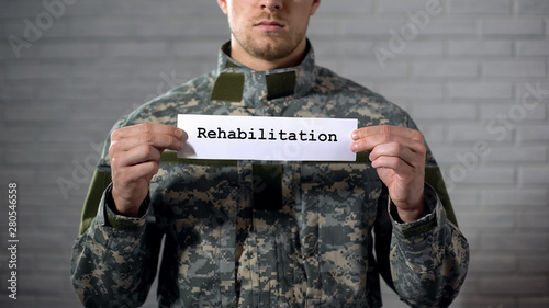 Rehabilitation word written on sign in hands of male soldier, health support