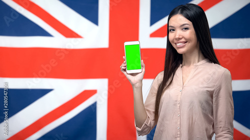 Lady showing phone with green screen against British flag on background, app