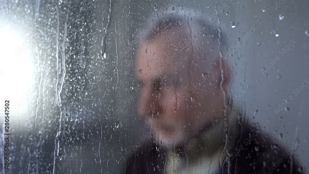 Sad male pensioner feeling lonely, rain drops window glass, melancholy, problem