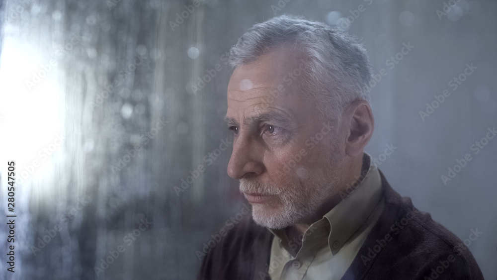 Fototapeta premium Senior man feeling sad, rain drops on window glass, depression concept, lonely