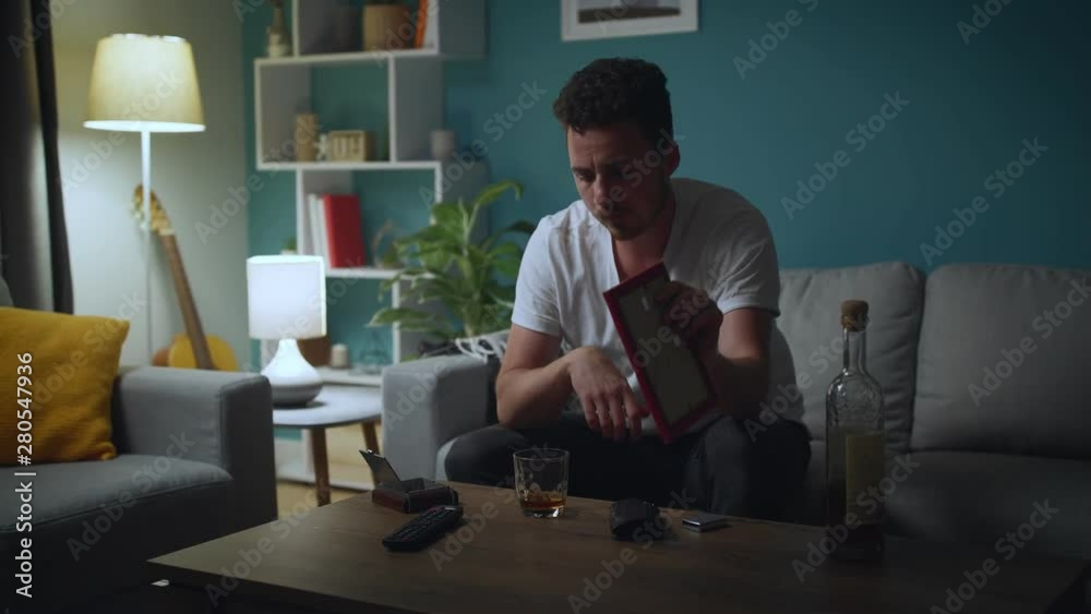 Sad man looking at photo of ex-girlfriend, regretting break-up and drink alcohol Sad man looking at photo of ex-girlfriend, regretting break-up and drink alcohol