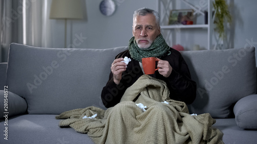 Ill pensioner sneezing and holding hot beverage, treating influenza, epidemic