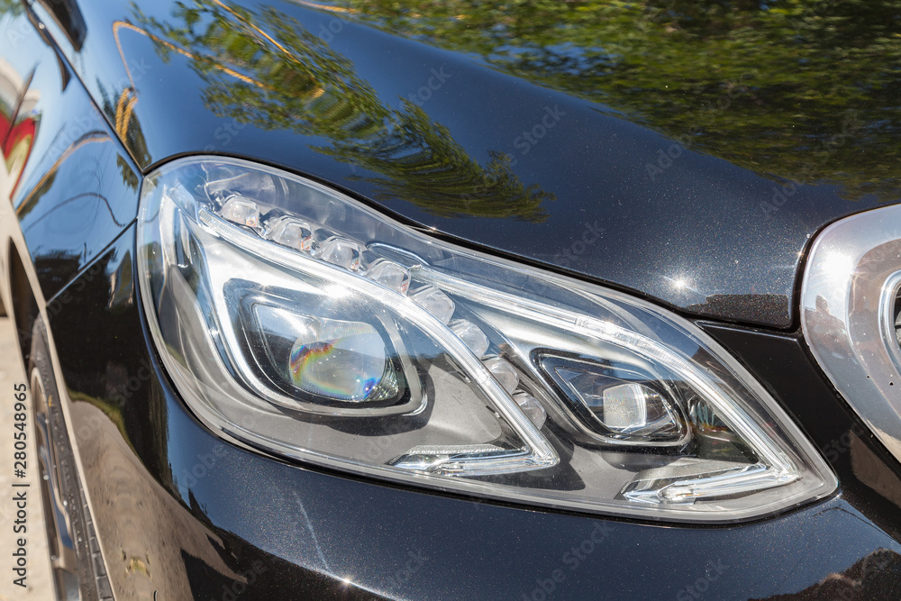 Black car front led headlight view with dark gray interior in excellent condition in a parking space near green tree