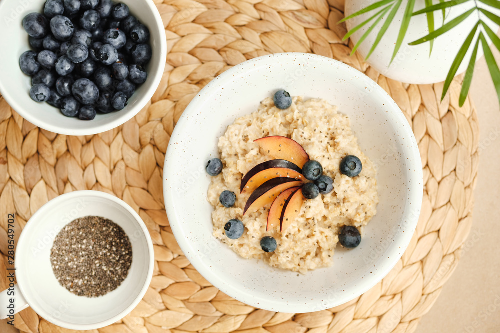 Oatmeal with blueberries, plums and chia seeds in a ceramic bowl on a wicker stand. Oatmeal with blueberries, plums and chia seeds in a ceramic bowl on a wicker stand.