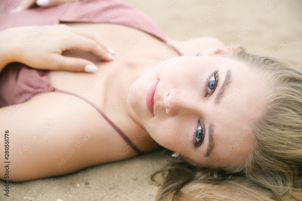 Obraz premium Young woman in pink dress lying on the sand and enjoys sea.