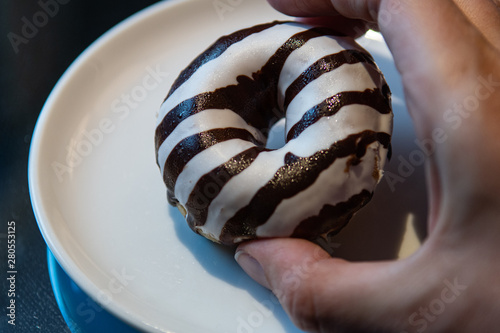 Right hand holding delicious tasty Zebra striped donut and white plate in background.