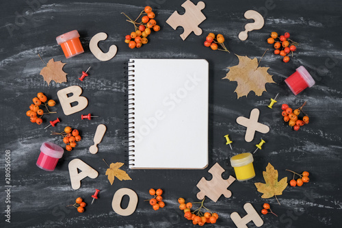 Back to school concept. Notebook, rowan, gouache and dried maple leaves and office supplies on black table background. Flat lay, top view, copy space.