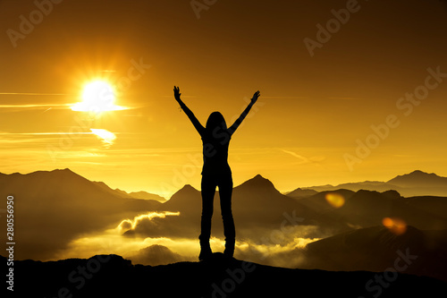 Frau in Siegerpose bei Sonnenaufgang auf einem Berggipfel