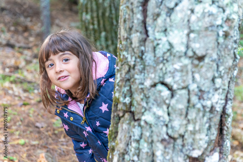 Young girl playing hide and seek behind a tree trunk