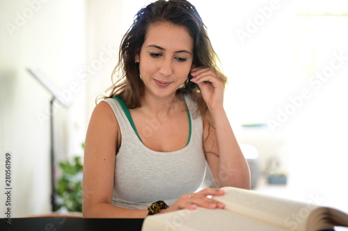 Handsome young woman sitting at a table and reading a book