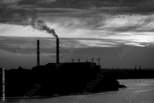 Sunset silhouette of industrial plant with a smoking pipe located on a river. © Volodymyr Herasymov