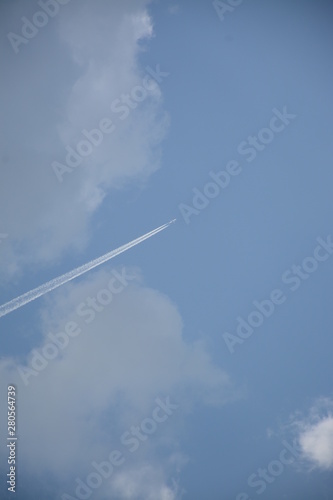 The plane soars up against the blue sky with clouds