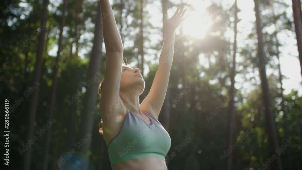 Pregnant woman doing meditating yoga outdoors on sunny day. Young expectant mother meditates practice stretching raising her hands up to the sun in green park with tall trees on background Pregnant woman doing meditating yoga outdoors on sunny day. Young expectant mother meditates practice stretching raising her hands up to the sun in green park with tall trees on background