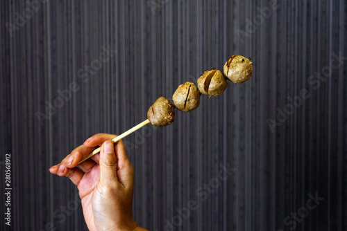 Asian female hand holding beef meatballs skewer on dark background