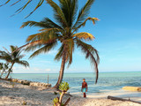 Man walking on the white beach and turquoise water with clear blue sky and lots of palm trees  on Sicsican Island in Balabac, Palawan, Philippines
