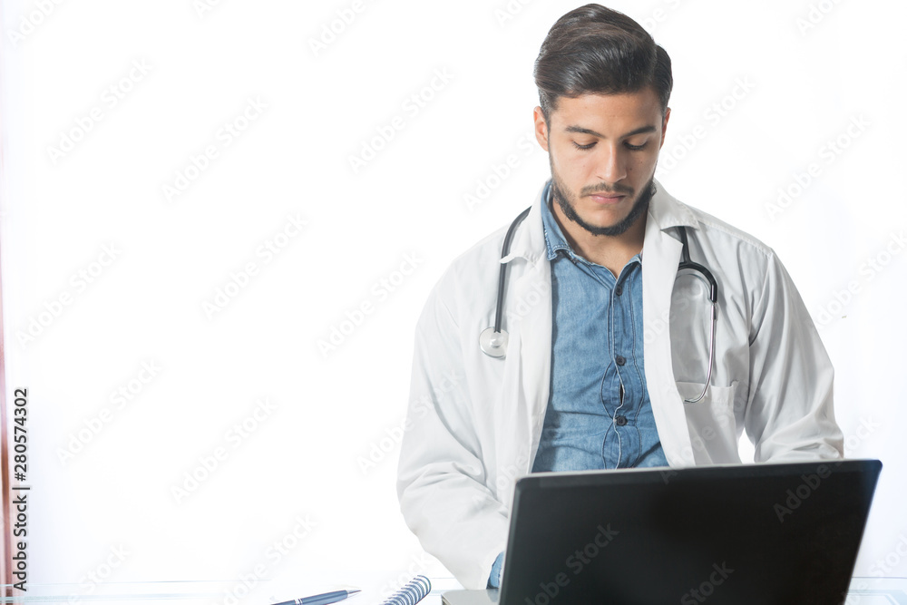 Young doctor poses for a portrait in studio. He is looking at computer while working at is desk. Young doctor poses for a portrait in studio. He is looking at computer while working at is desk.