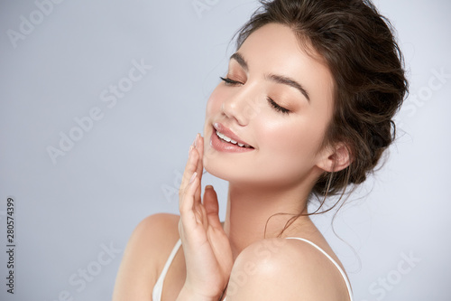 young and happy girl with light make-up and closed eyes touching her chin and smiling
