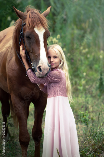 innocent blonde girl with horse in forest. beautiful Caucasian girl with long blonde hair in a pink dress hugs a brown horse. innocent childhood concept. natural beauty. hipster style.