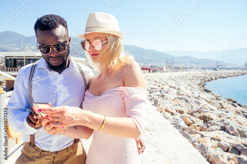 caucasian young woman with mixed-race african american male looking at smartphone route gps navigator at summer vacation in Turkey © yurakrasil
