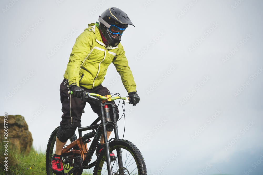 Aged male athlete in helmet and mask rides down a grassy slope on a mountain bike. Downhill mountain bike concept Aged male athlete in helmet and mask rides down a grassy slope on a mountain bike. Downhill mountain bike concept