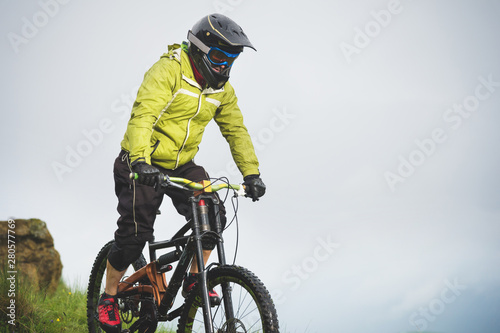 Aged male athlete in helmet and mask rides down a grassy slope on a mountain bike. Downhill mountain bike concept