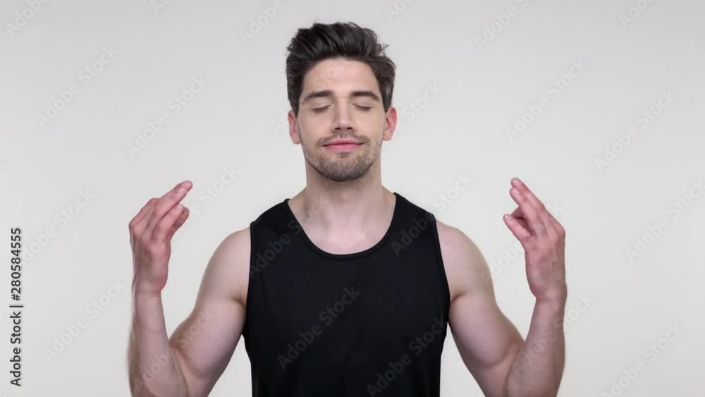 Calm young bearded sporty man in black shirt meditating with closed eyes over gray background isolated Calm young bearded sporty man in black shirt meditating with closed eyes over gray background isolated